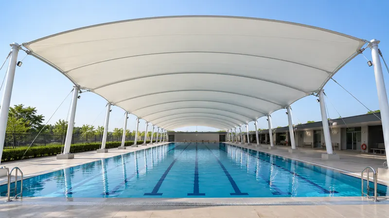 Barrel-vault tensile canopy covering an outdoor lap pool