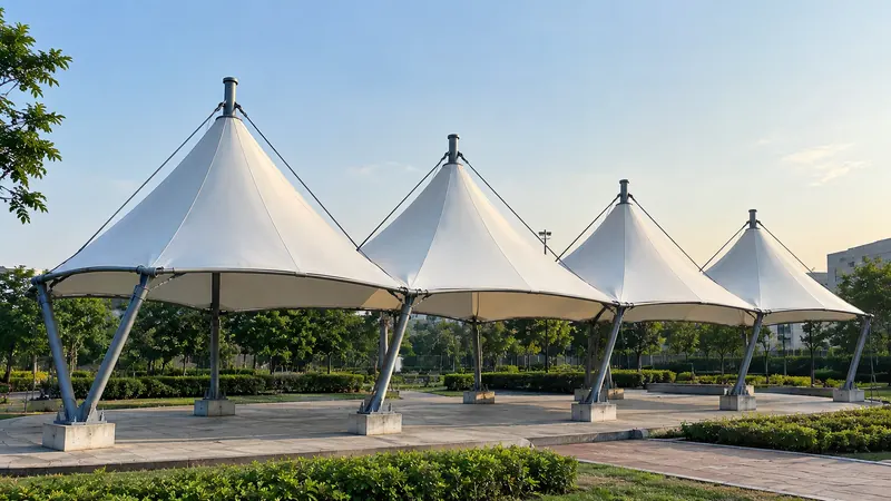 Row of four conical tensile canopies over a park plaza at dusk
