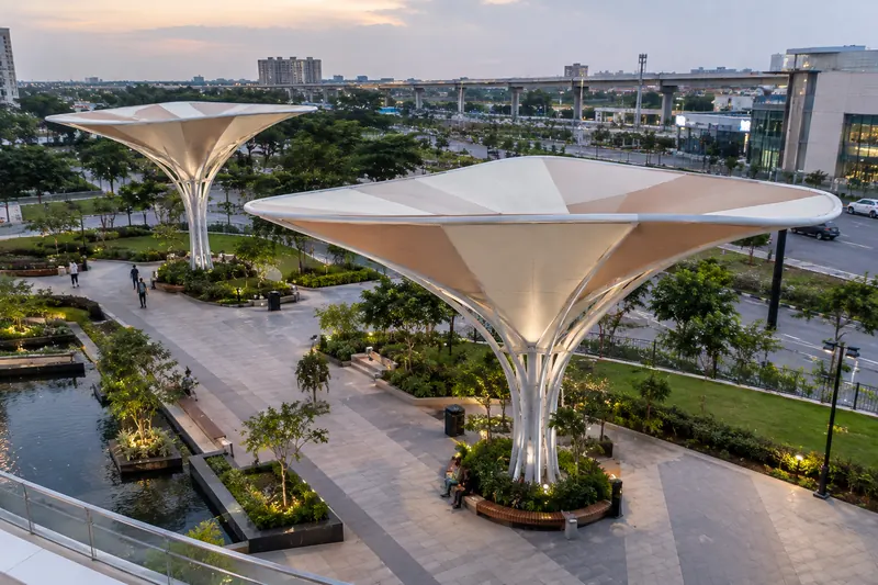 Pair of inverted umbrella tensile canopies over a riverside plaza at dusk
